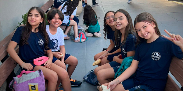 Alunos sorrindo sentadas no chão da escola 