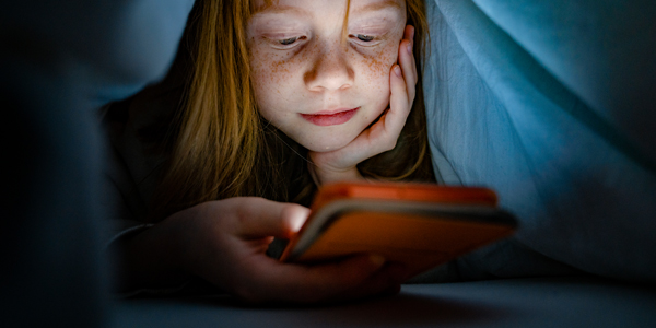 menina de aproximadamente 9 anos embaixo do cobertor, olhando o celular