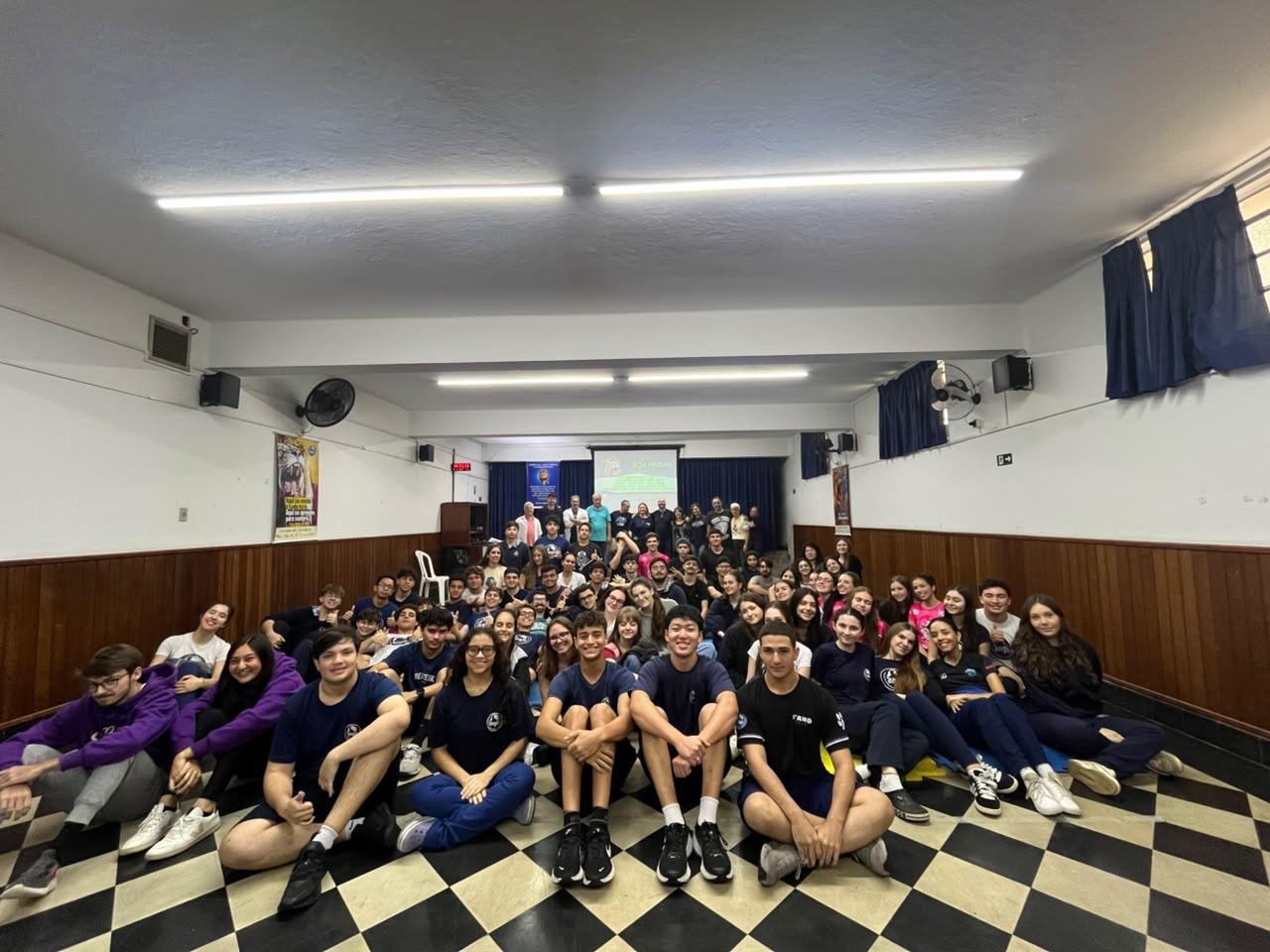 Grupo de alunos reunidos em um auditório escolar, posando para uma foto coletiva.